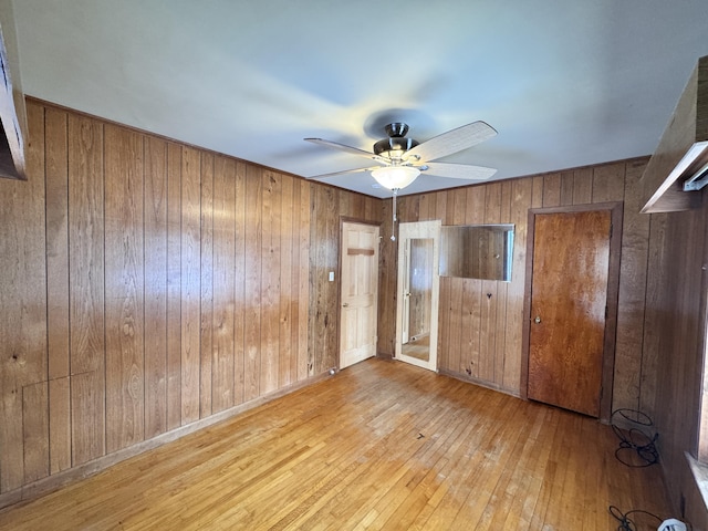 unfurnished bedroom with baseboards, wood walls, hardwood / wood-style flooring, and a ceiling fan