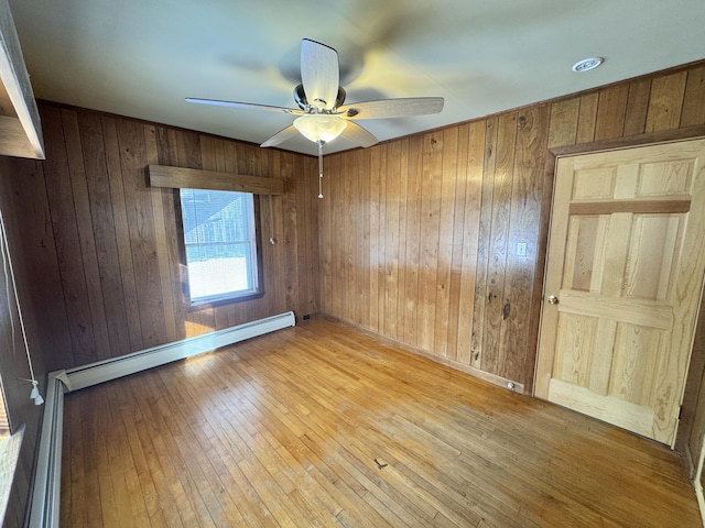 empty room with a baseboard heating unit, baseboards, hardwood / wood-style flooring, and a ceiling fan