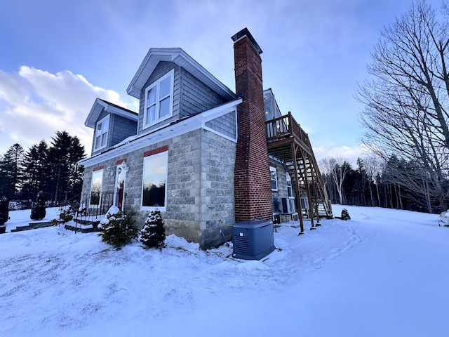 view of snow covered exterior featuring stone siding, a chimney, stairway, and cooling unit