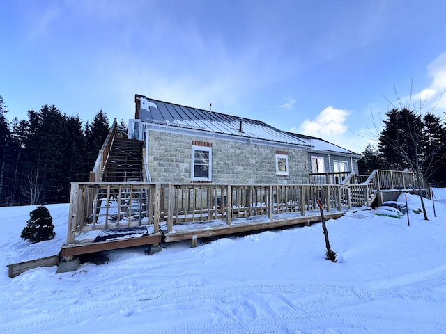 snow covered back of property featuring a standing seam roof, metal roof, stone siding, a wooden deck, and stairs