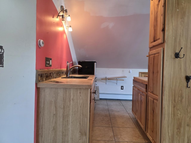 kitchen with light tile patterned floors, baseboard heating, a sink, and lofted ceiling