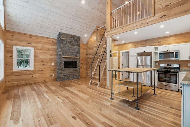 kitchen with appliances with stainless steel finishes, wooden walls, a fireplace, white cabinetry, and light stone countertops