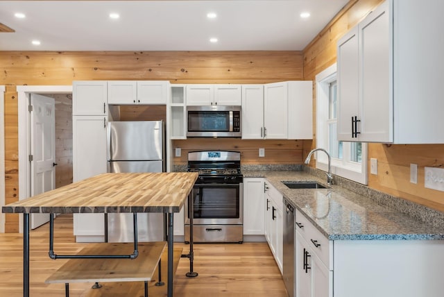 kitchen with sink, white cabinets, light stone counters, stainless steel appliances, and light hardwood / wood-style flooring