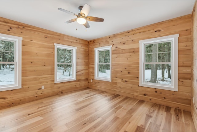 unfurnished room featuring wood walls, ceiling fan, and light hardwood / wood-style flooring