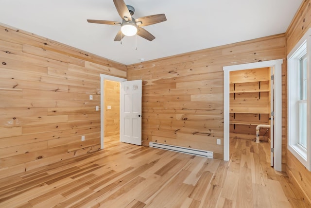 empty room with a baseboard heating unit, wooden walls, hardwood / wood-style floors, and ceiling fan