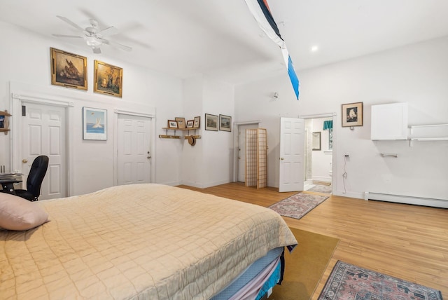 bedroom featuring a baseboard heating unit, ensuite bath, ceiling fan, and light wood-type flooring