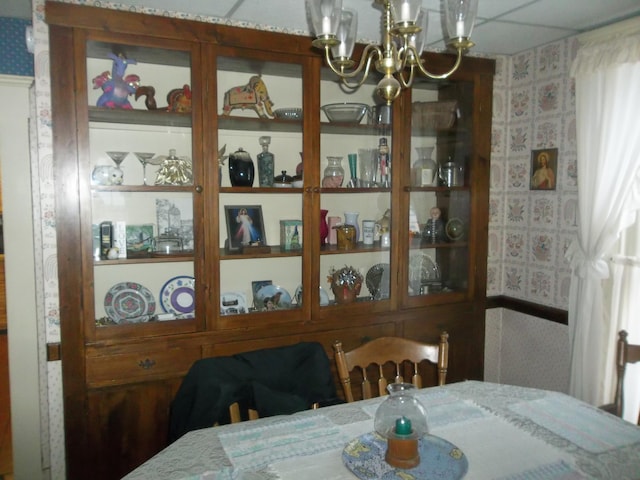 dining space with a drop ceiling, wallpapered walls, and an inviting chandelier