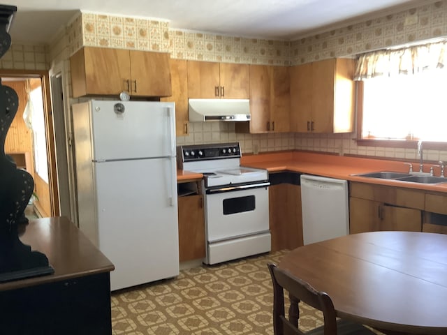 kitchen with light floors, backsplash, a sink, white appliances, and under cabinet range hood