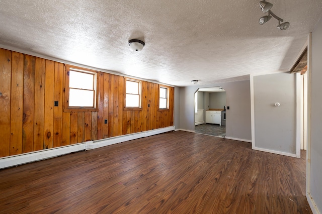 unfurnished room with a baseboard heating unit, a textured ceiling, dark hardwood / wood-style flooring, and wood walls