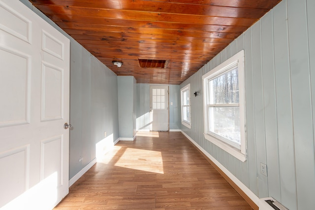 hallway with wooden walls, wooden ceiling, and light hardwood / wood-style floors