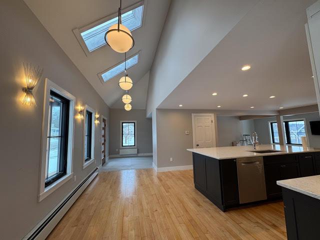 kitchen featuring sink, dishwasher, baseboard heating, decorative light fixtures, and light wood-type flooring