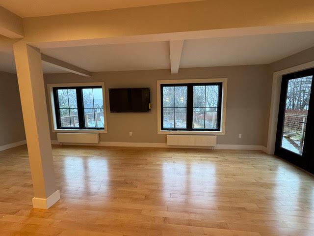 unfurnished living room with light wood-type flooring, radiator heating unit, and beam ceiling