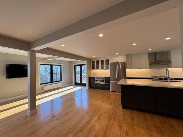 kitchen featuring wall chimney range hood, sink, stainless steel fridge, white cabinets, and light wood-type flooring