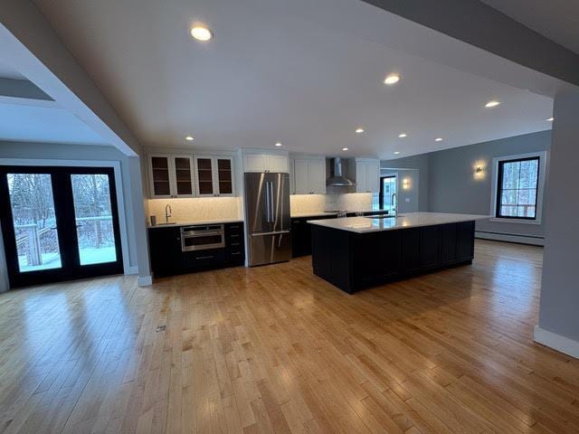 kitchen with a kitchen island, tasteful backsplash, stainless steel fridge, a baseboard heating unit, and wall chimney exhaust hood