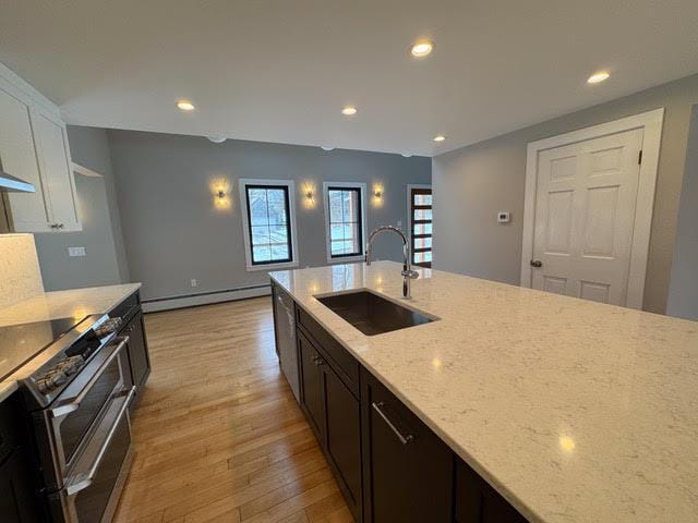 kitchen with sink, baseboard heating, white cabinetry, double oven range, and light stone counters