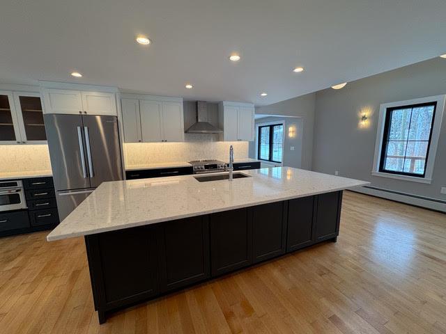 kitchen with sink, appliances with stainless steel finishes, white cabinetry, a spacious island, and wall chimney exhaust hood