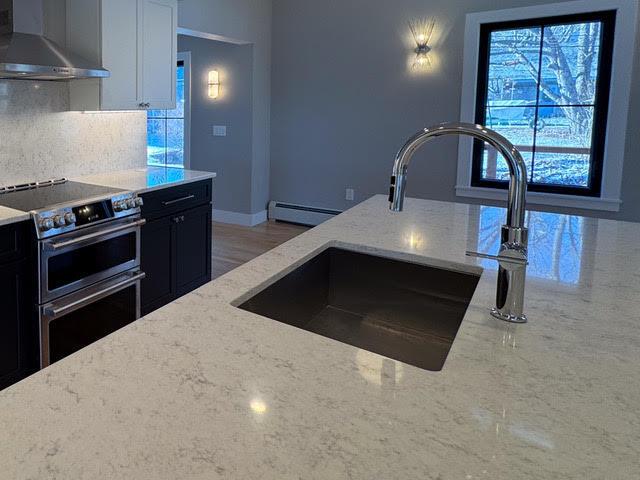 kitchen featuring plenty of natural light, wall chimney range hood, light stone countertops, range with two ovens, and white cabinets