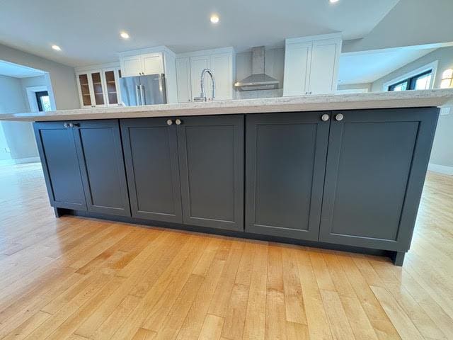 kitchen featuring a spacious island, light hardwood / wood-style floors, wall chimney exhaust hood, and white cabinets