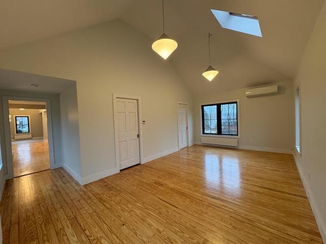 unfurnished living room featuring light hardwood / wood-style floors, a skylight, high vaulted ceiling, and an AC wall unit