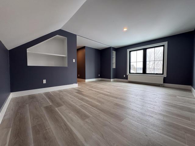 interior space featuring built in shelves, vaulted ceiling, and light hardwood / wood-style floors