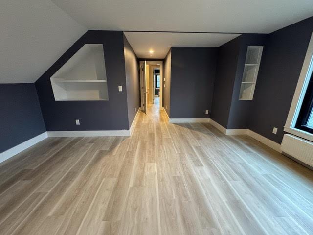 bonus room with built in shelves, lofted ceiling, light hardwood / wood-style flooring, and radiator heating unit