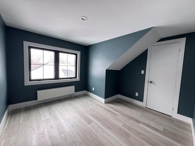 additional living space featuring radiator, vaulted ceiling, and light wood-type flooring