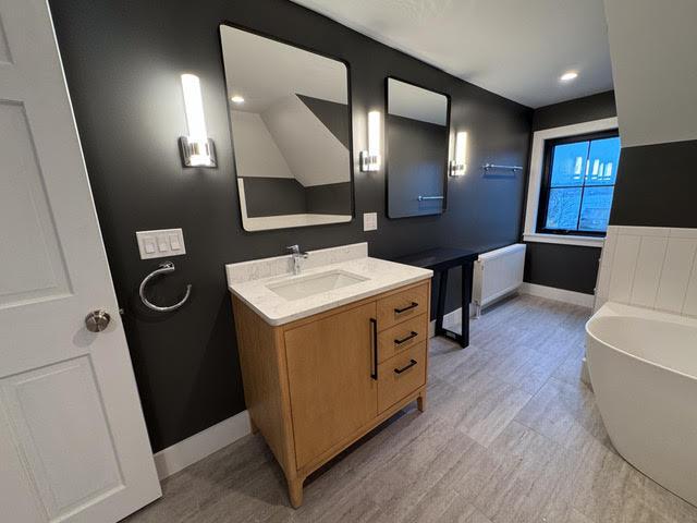 bathroom featuring a washtub, radiator, and vanity