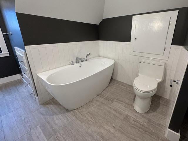 bathroom featuring a washtub, tile walls, and toilet