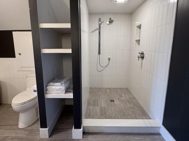 bathroom featuring wood-type flooring, a tile shower, tile walls, and toilet