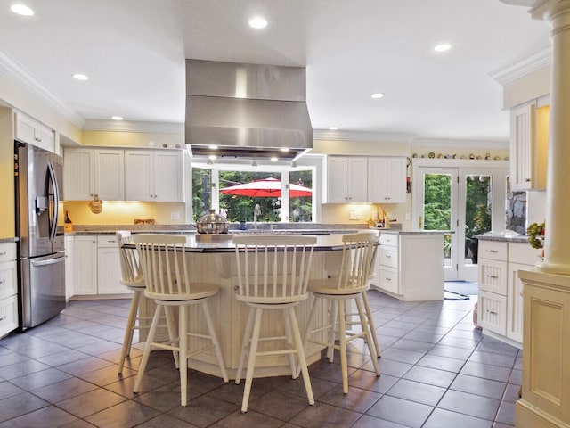 kitchen with white cabinetry, a kitchen breakfast bar, island range hood, a kitchen island, and stainless steel fridge with ice dispenser