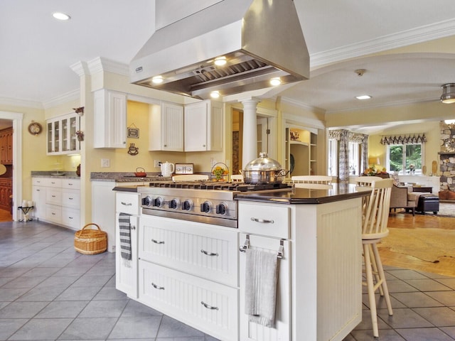 kitchen with light tile patterned flooring, white cabinetry, a center island with sink, a kitchen breakfast bar, and range hood