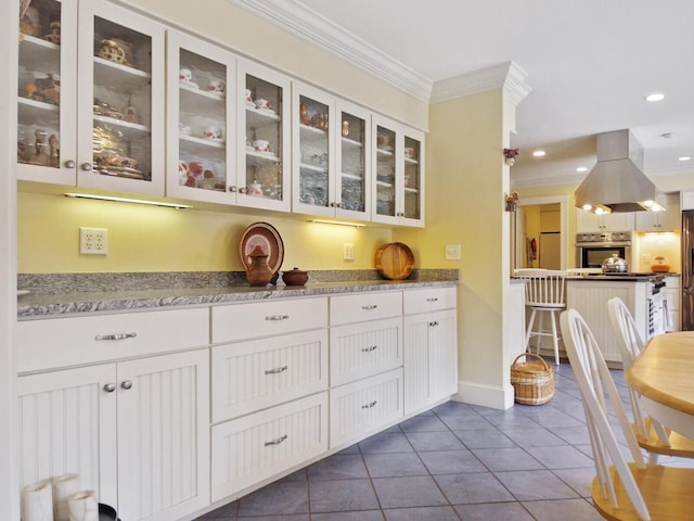 kitchen with island range hood, white cabinetry, dark tile patterned floors, stainless steel appliances, and crown molding