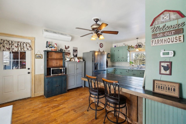 kitchen featuring appliances with stainless steel finishes, light hardwood / wood-style flooring, a wall mounted air conditioner, ceiling fan, and kitchen peninsula