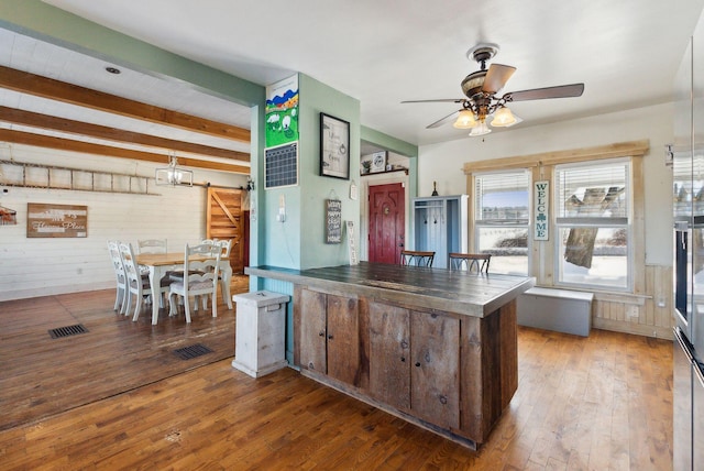 kitchen featuring wood-type flooring, ceiling fan, a barn door, dark brown cabinetry, and beam ceiling