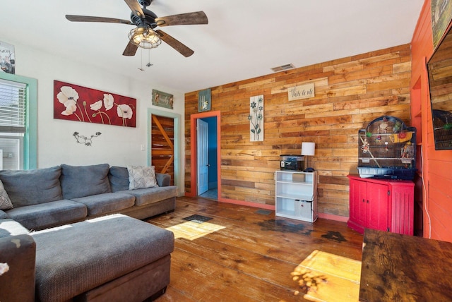 living room with hardwood / wood-style flooring, wooden walls, and ceiling fan