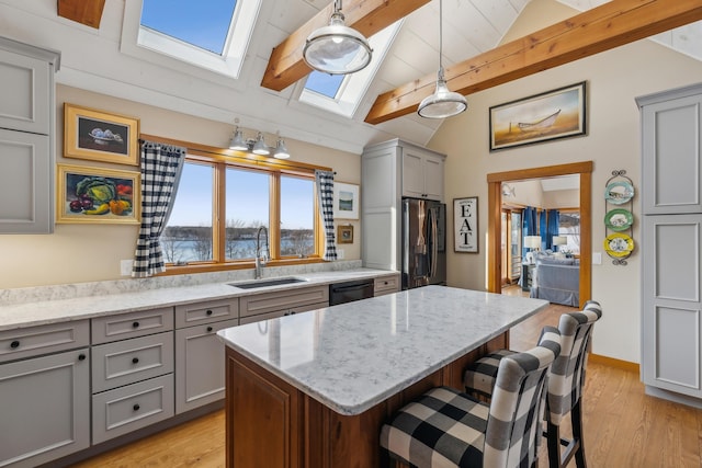 kitchen featuring sink, stainless steel fridge, hanging light fixtures, a center island, and vaulted ceiling with skylight