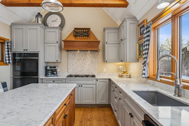 kitchen featuring sink, light stone counters, beamed ceiling, light hardwood / wood-style floors, and black appliances