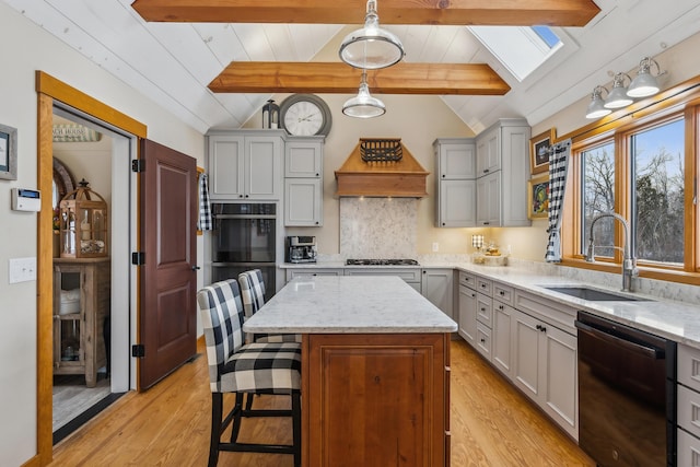 kitchen with sink, hanging light fixtures, vaulted ceiling with skylight, black appliances, and a kitchen island