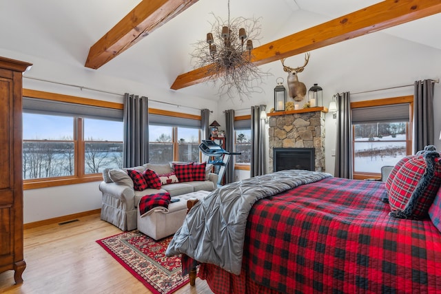 bedroom with a stone fireplace, a notable chandelier, high vaulted ceiling, and light hardwood / wood-style flooring