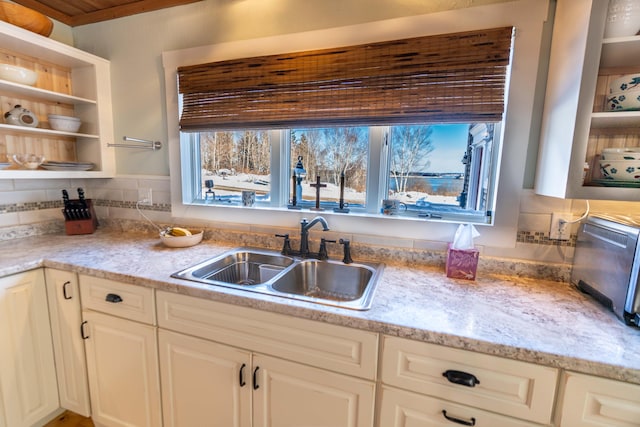 kitchen featuring tasteful backsplash, white cabinetry, light stone countertops, and sink