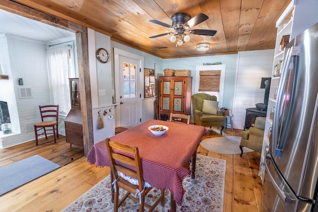 dining space with a wood stove, wooden ceiling, ceiling fan, and light wood-type flooring