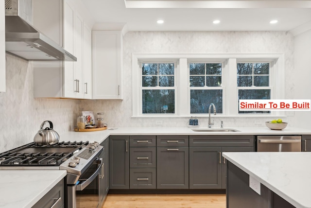 kitchen featuring white cabinetry, sink, light stone counters, stainless steel appliances, and wall chimney exhaust hood