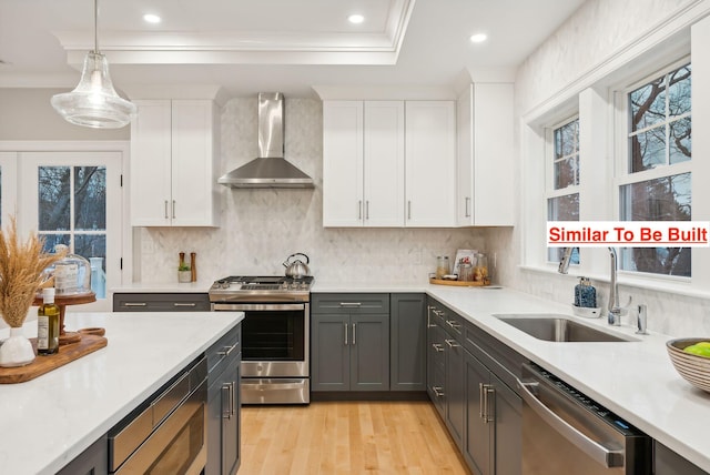 kitchen featuring pendant lighting, sink, white cabinets, stainless steel appliances, and wall chimney range hood