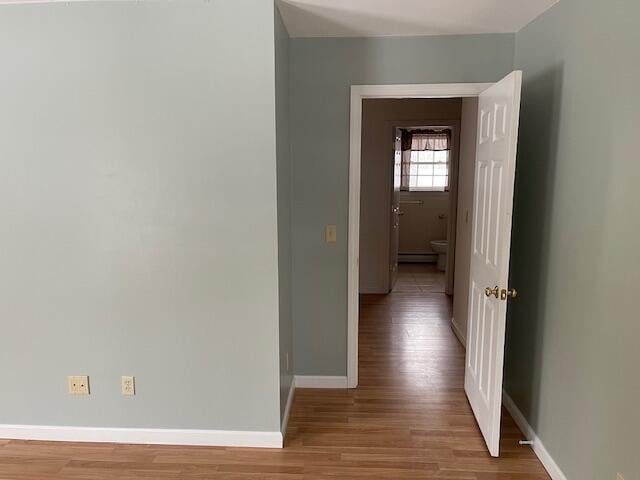 hall with light wood-type flooring, a baseboard radiator, and baseboards