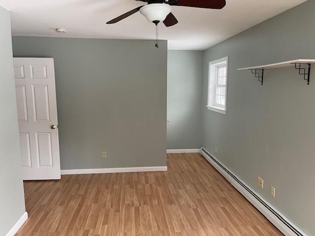 spare room featuring light wood finished floors, baseboards, baseboard heating, and a ceiling fan