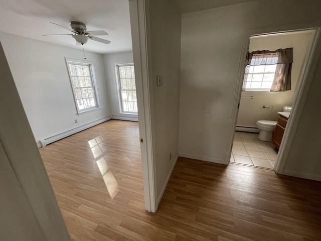 corridor with light wood finished floors, a baseboard radiator, and baseboards