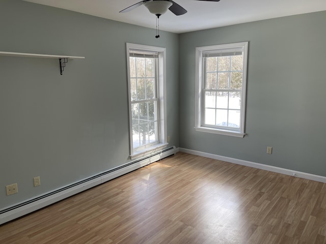 spare room featuring a baseboard heating unit, light wood finished floors, a ceiling fan, and baseboards