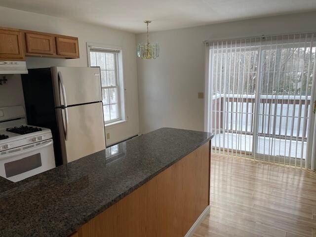 kitchen featuring under cabinet range hood, brown cabinets, dark stone counters, gas range gas stove, and pendant lighting