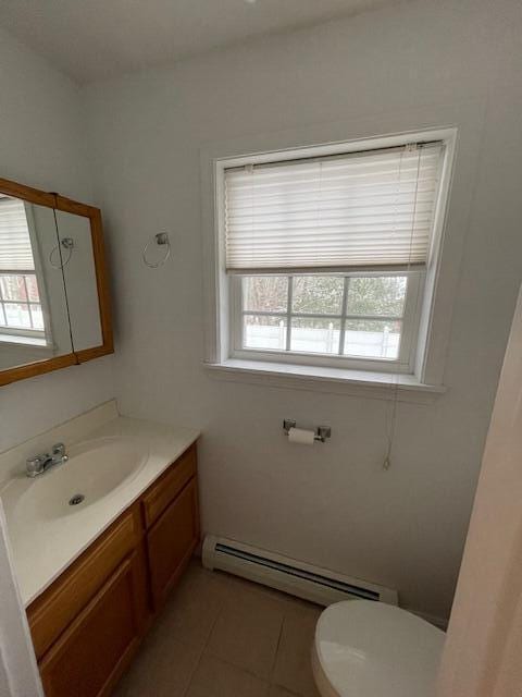 half bathroom with toilet, tile patterned flooring, a baseboard heating unit, and vanity