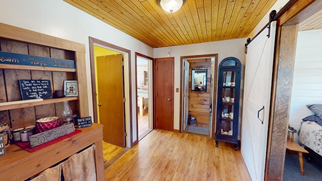 hall with a barn door, wood ceiling, and light hardwood / wood-style floors